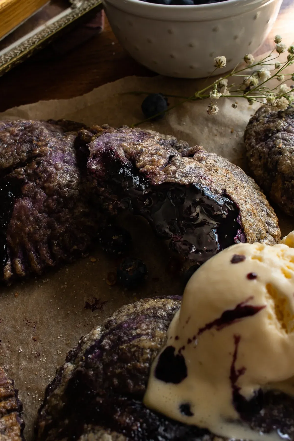 Close angled view of a broken-open Ube and Blueberry Mini Pie on parchment paper on a dark wooden board