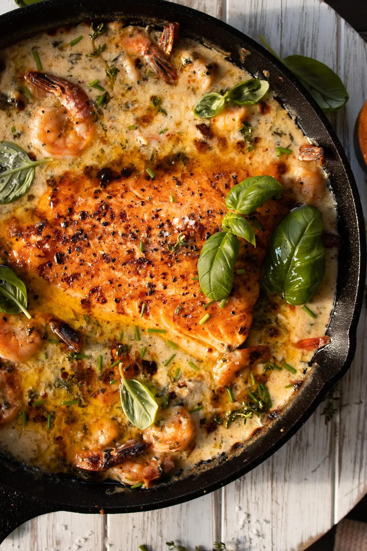 Overhead close-up of the black cast iron skillet of Saucy Salmon and Shrimp in Coconut Milk showing the whole seared salmon fillet with its vibrant orange-red sear and cracked black pepper