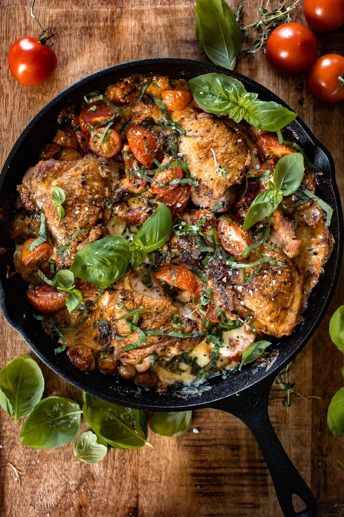 Full overhead view of a black cast iron skillet with handle containing caprese chicken thighs