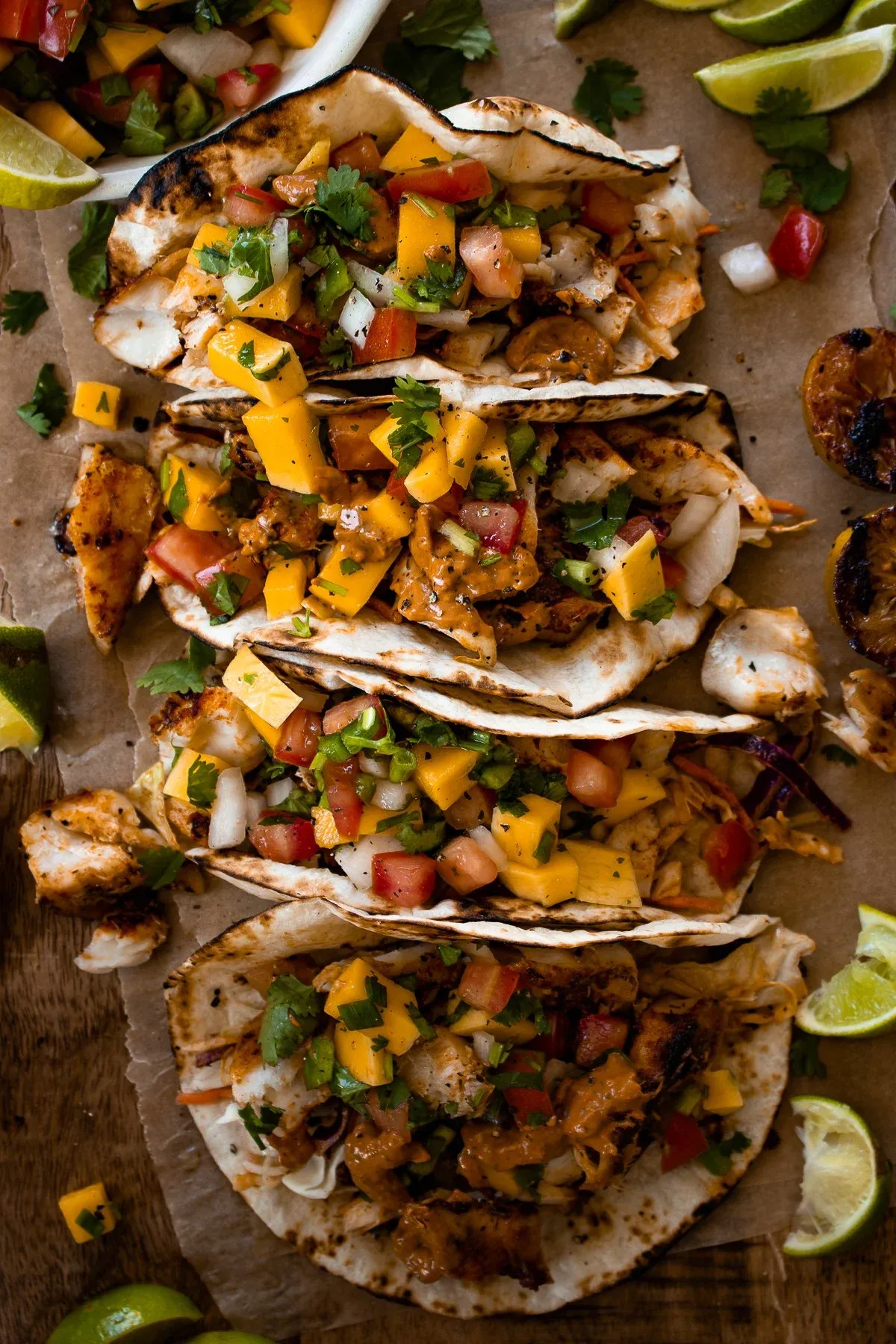 Slightly elevated overhead shot of four Caribbean fish tacos on crinkled parchment paper on a wooden board