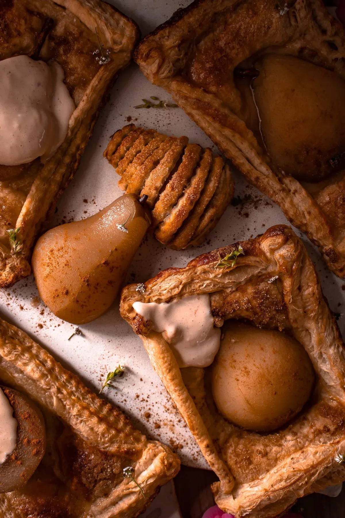Close-up overhead of assembled poached pear pastry tarts on a white surface showing contrasting preparations