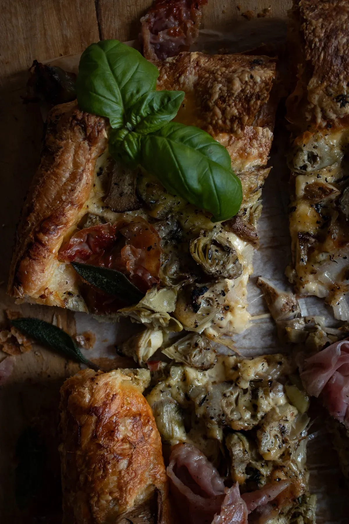 Angled close-up of baked Artichoke and Mushroom Tart sections showing bubbling melted cheese, golden-brown flaky pastry crust