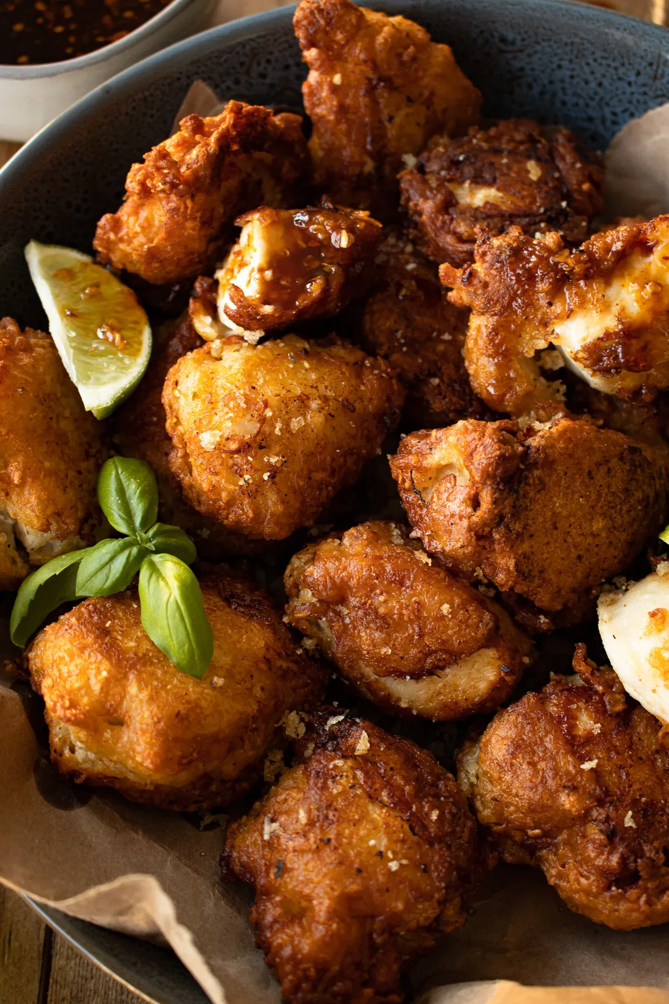 Close-up angled shot of piled Batter Fried Chicken in the dark blue bowl showing the rough-textured spiced batter crust in deep amber and golden tones