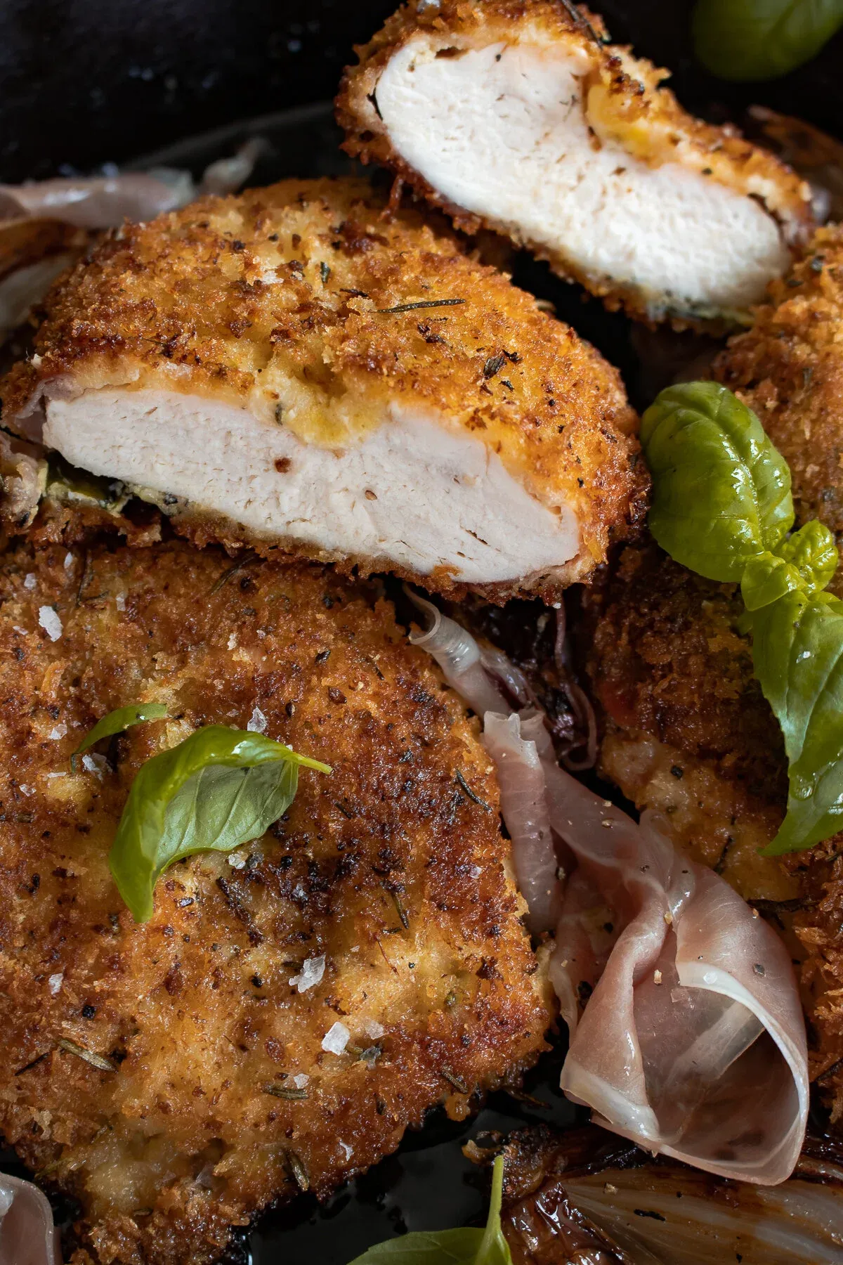 Close-up cross-section of a sliced Prosciutto and Basil Wrapped Chicken cutlet in the cast iron showing the juicy white