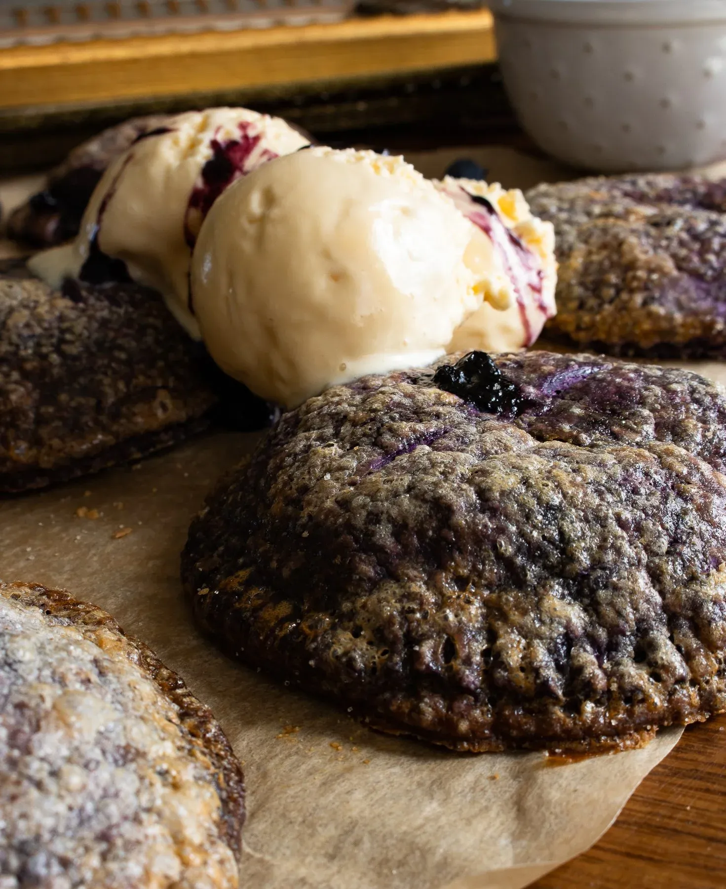 Low-angle side view of an Ube and Blueberry Mini Pie on parchment on a dark wooden board