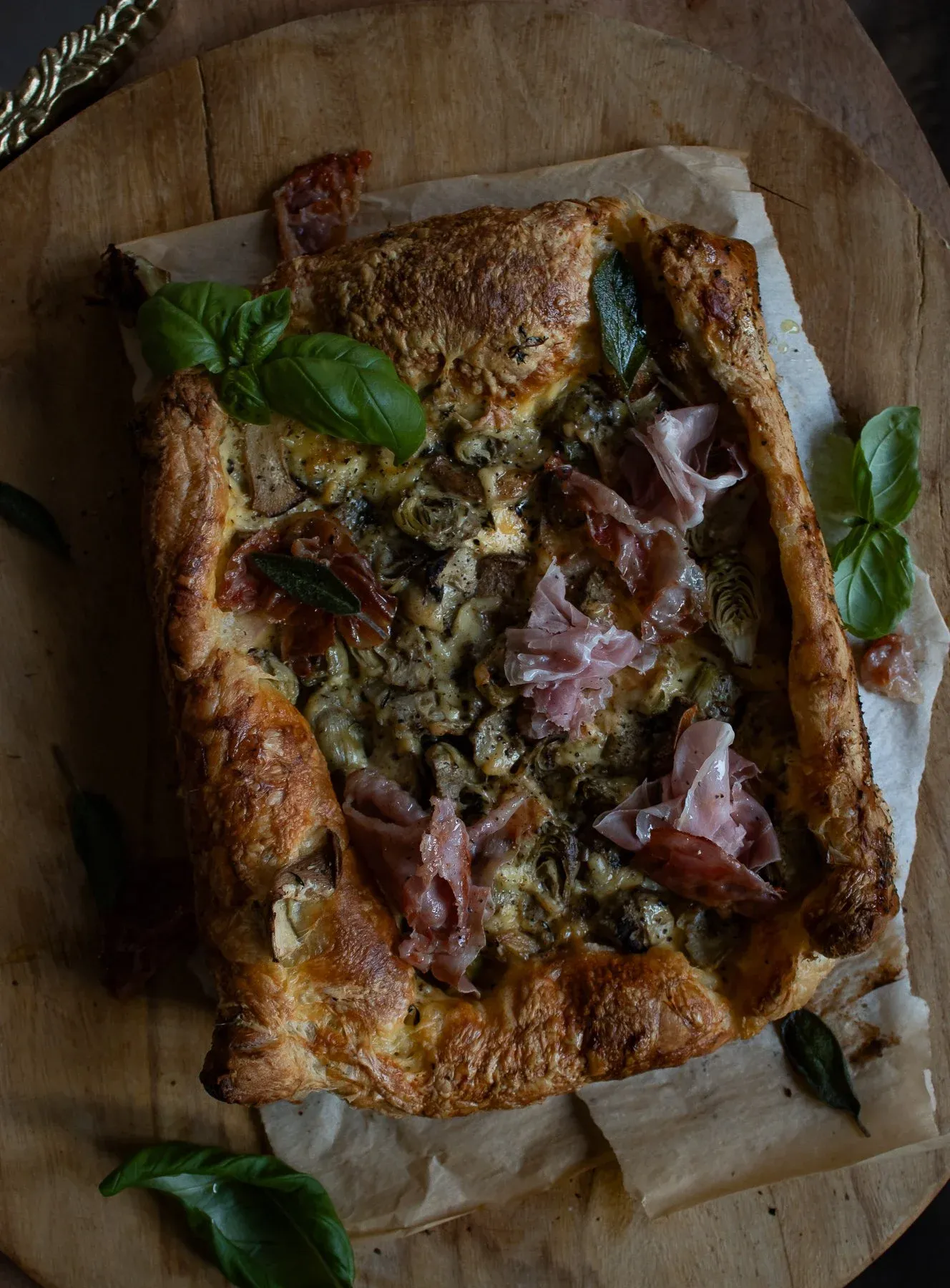 Overhead view of the whole baked Artichoke and Mushroom Tart on parchment atop a round wooden board