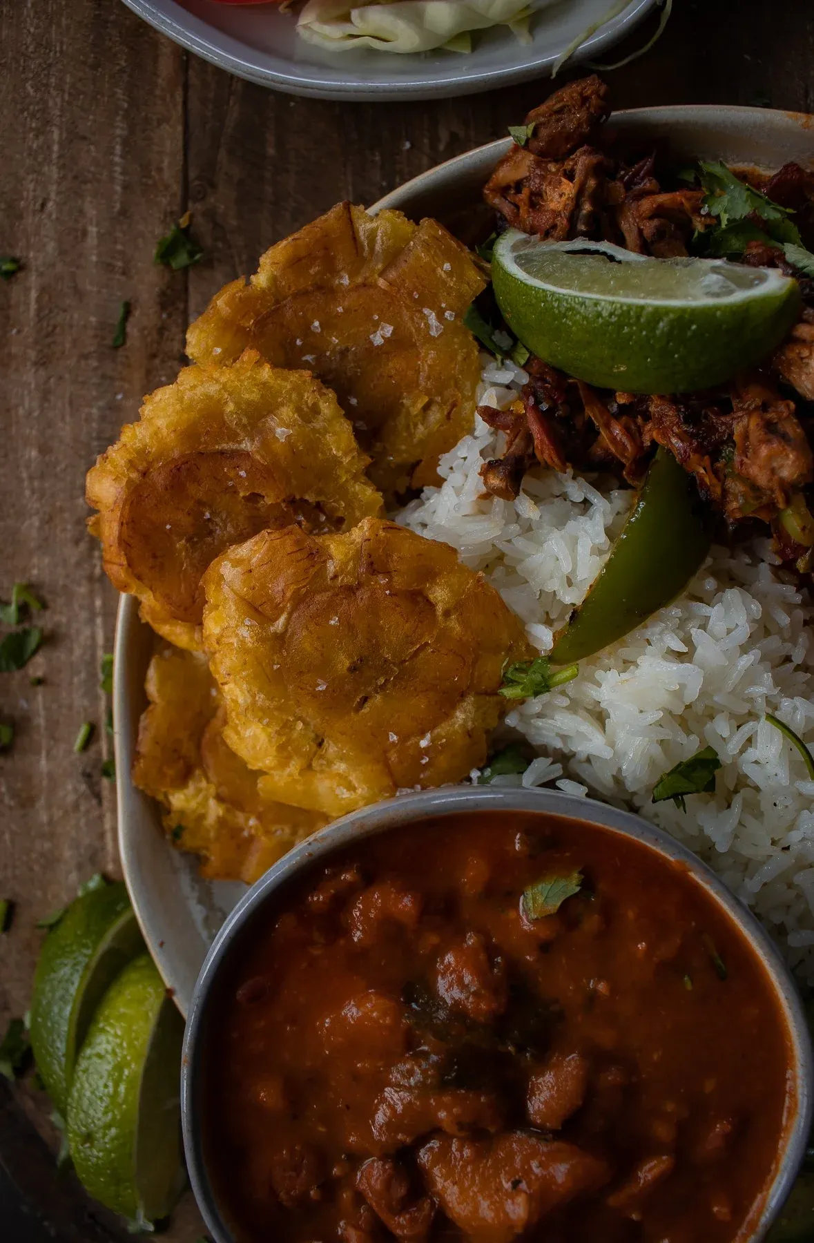 Angled close-up of the tostones (twice-fried smashed green plantain discs) in golden-crispy detail at the front of the La Bandera Dominicana plate