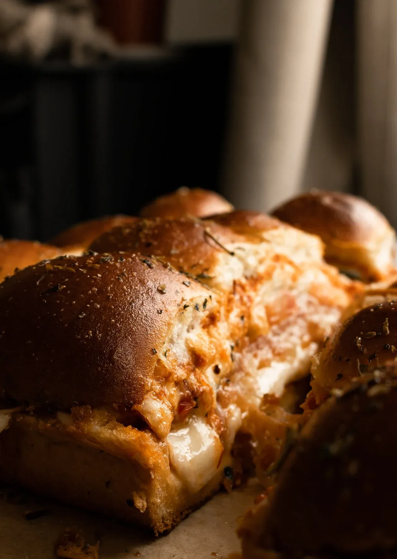 Side close-up of prosciutto and cheese pull-apart sliders with one slider lifted to show the cross-section
