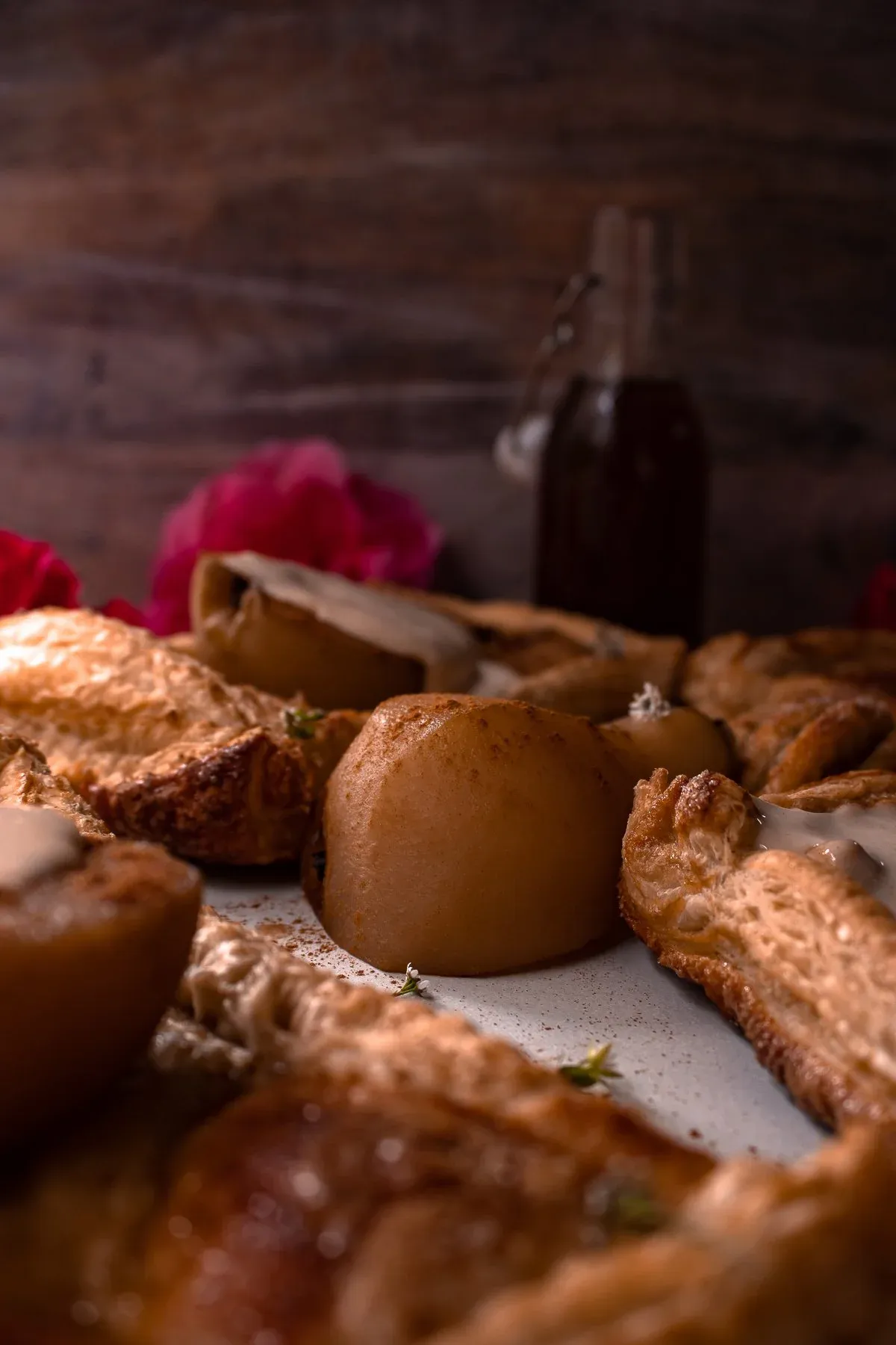Side-angle view of poached pear pastry tarts on a white ceramic surface with dramatic dark background