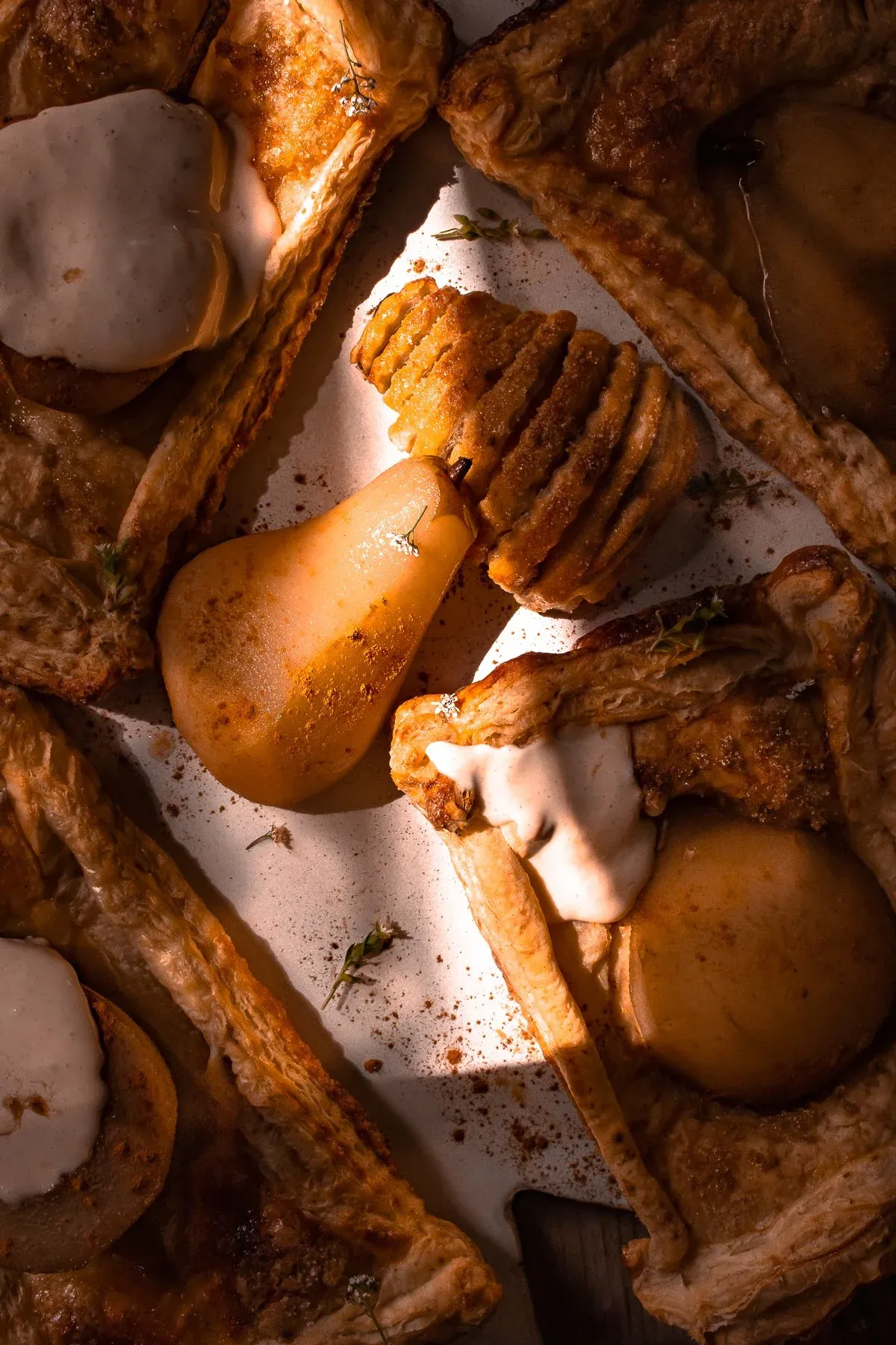 Overhead warm-lit shot of multiple poached pear pastry tarts with mascarpone cream on a white surface