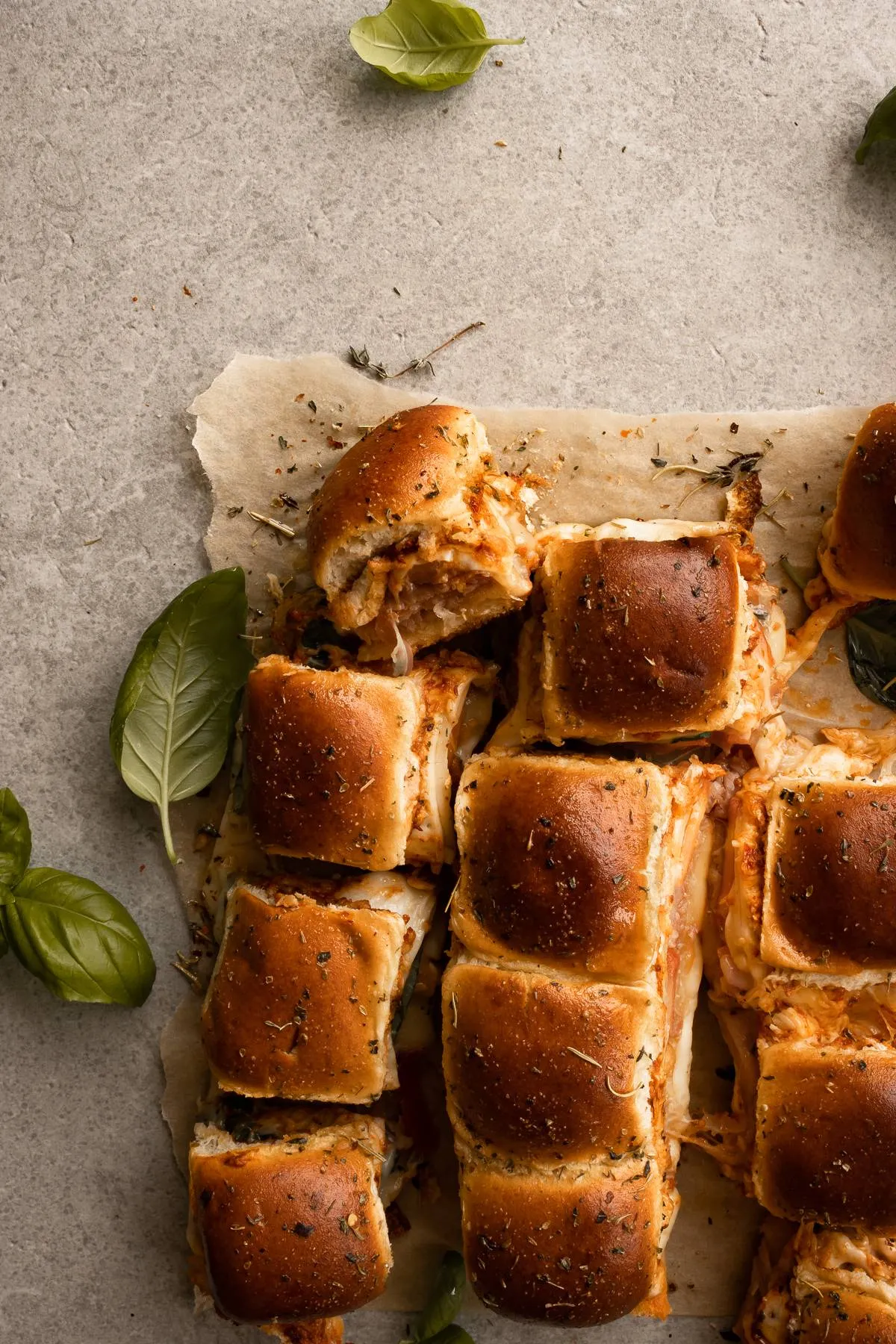 Overhead flat-lay of prosciutto and cheese pull-apart sliders on parchment paper on a light gray surface