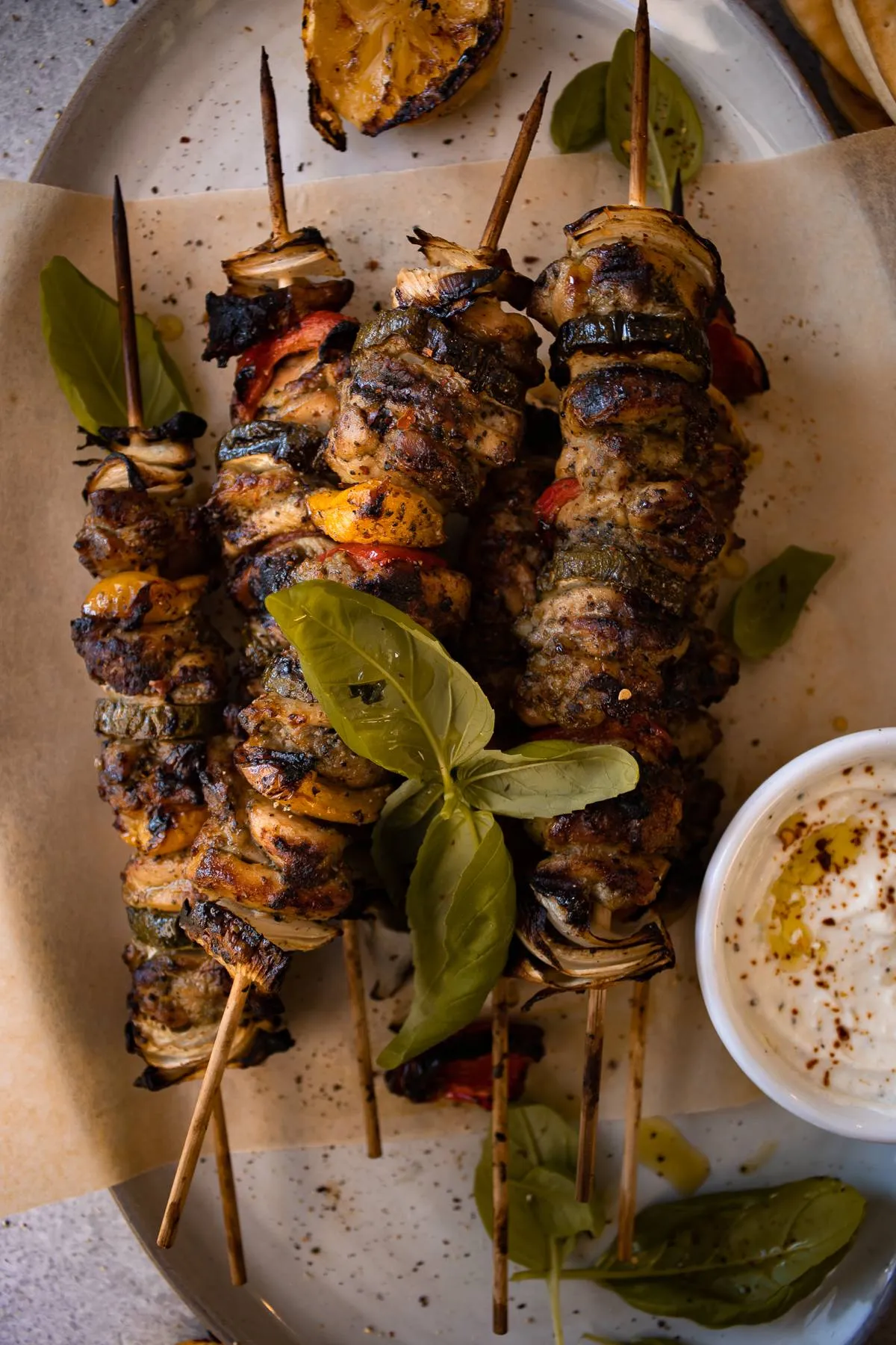Three Grilled Chicken Skewers with Garlicky Whipped Ricotta on an oval white ceramic platter lined with parchment