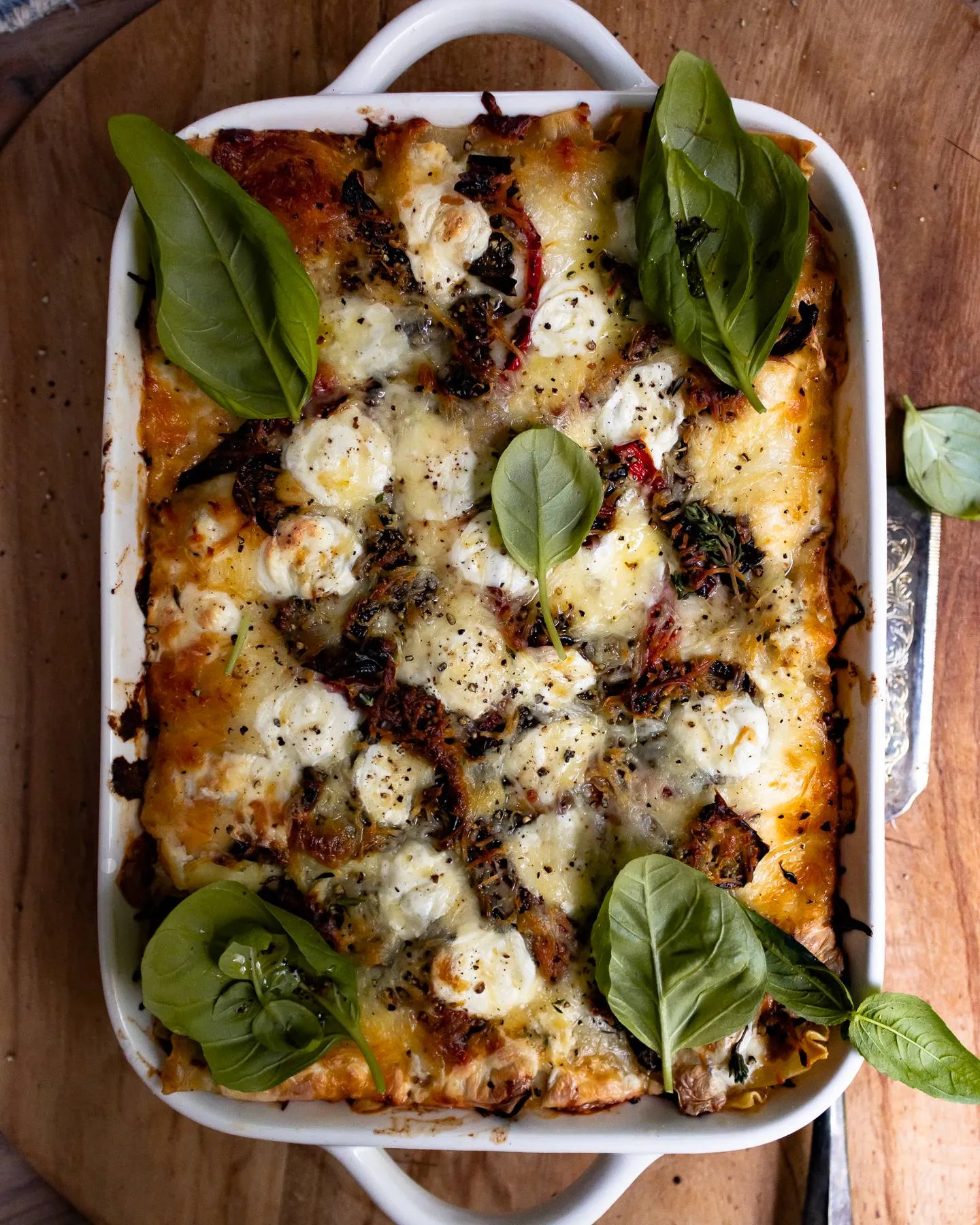 Spicy Chicken and Spinach Lasagna in a white ceramic rectangular baking dish with handles, overhead view on a wooden board