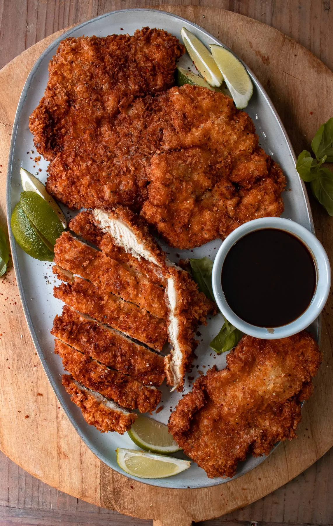 Overhead view of two large mojo chicken katsu cutlets on a grey oval ceramic platter on a round wooden cutting board