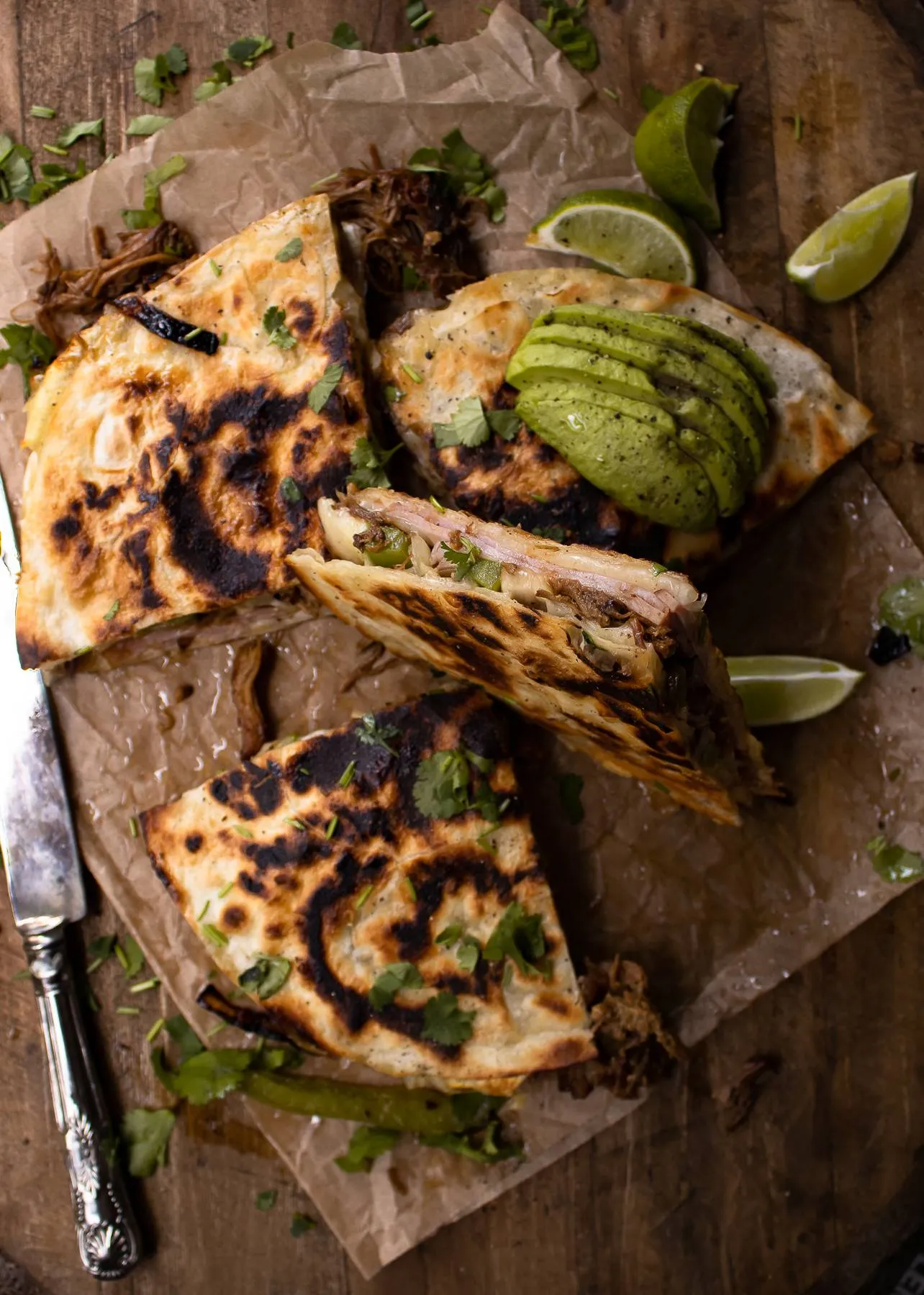 Overhead view of Cubano Inspired Quesadilla cut into quarters on crumpled parchment paper over a dark wood board