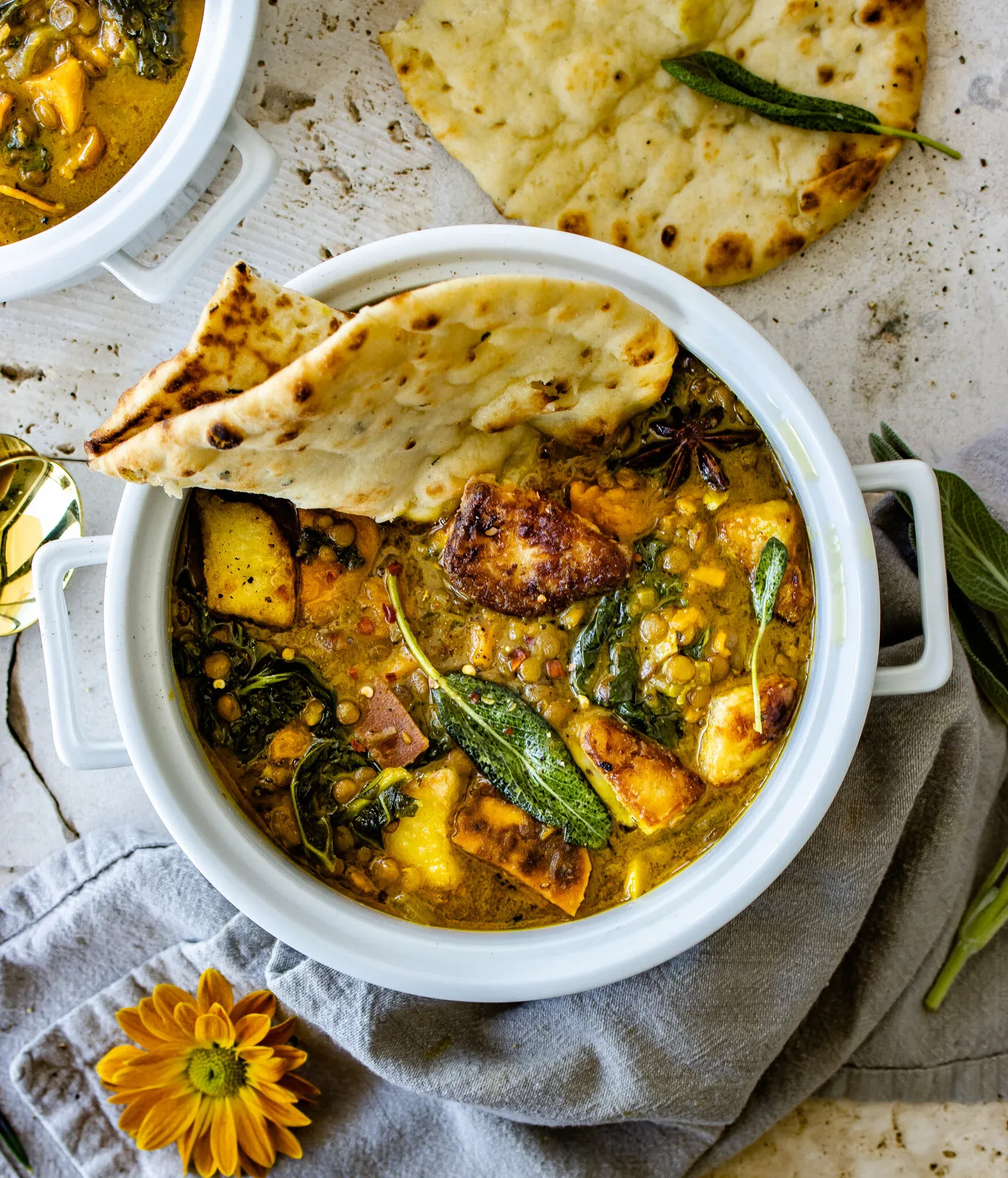 Overhead close-up of a white ceramic casserole pot filled with golden-yellow sweet potato and lentil soup with fried halloumi