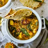 Overhead close-up of a white ceramic casserole pot filled with golden-yellow sweet potato and lentil soup with fried halloumi