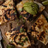 Overhead view of Cubano Inspired Quesadilla cut into quarters on crumpled parchment paper over a dark wood board