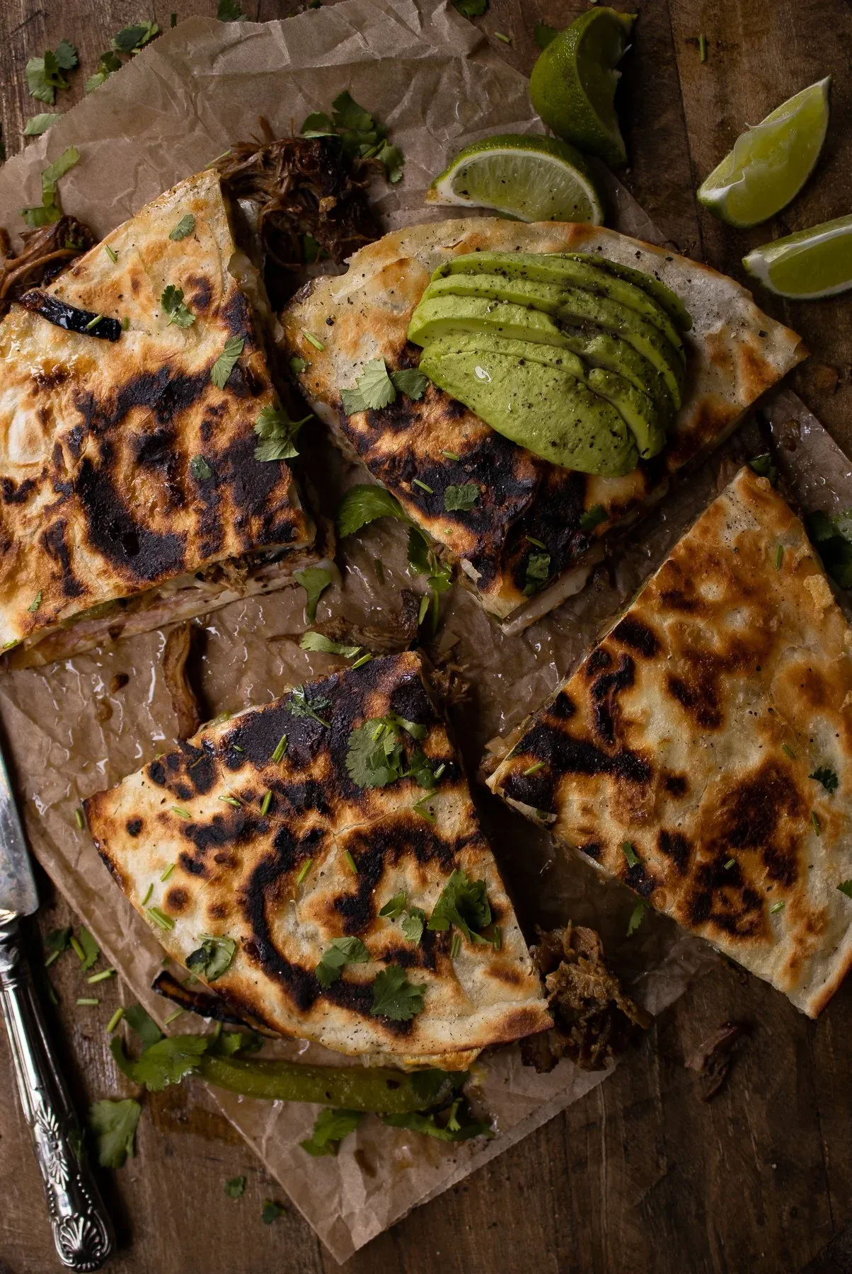 Overhead view of Cubano Inspired Quesadilla cut into quarters on crumpled parchment paper over a dark wood board