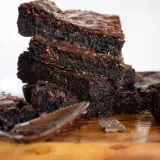 Stack of four Vegan Dark Chocolate Brownies balanced on a live-edge wood cutting board