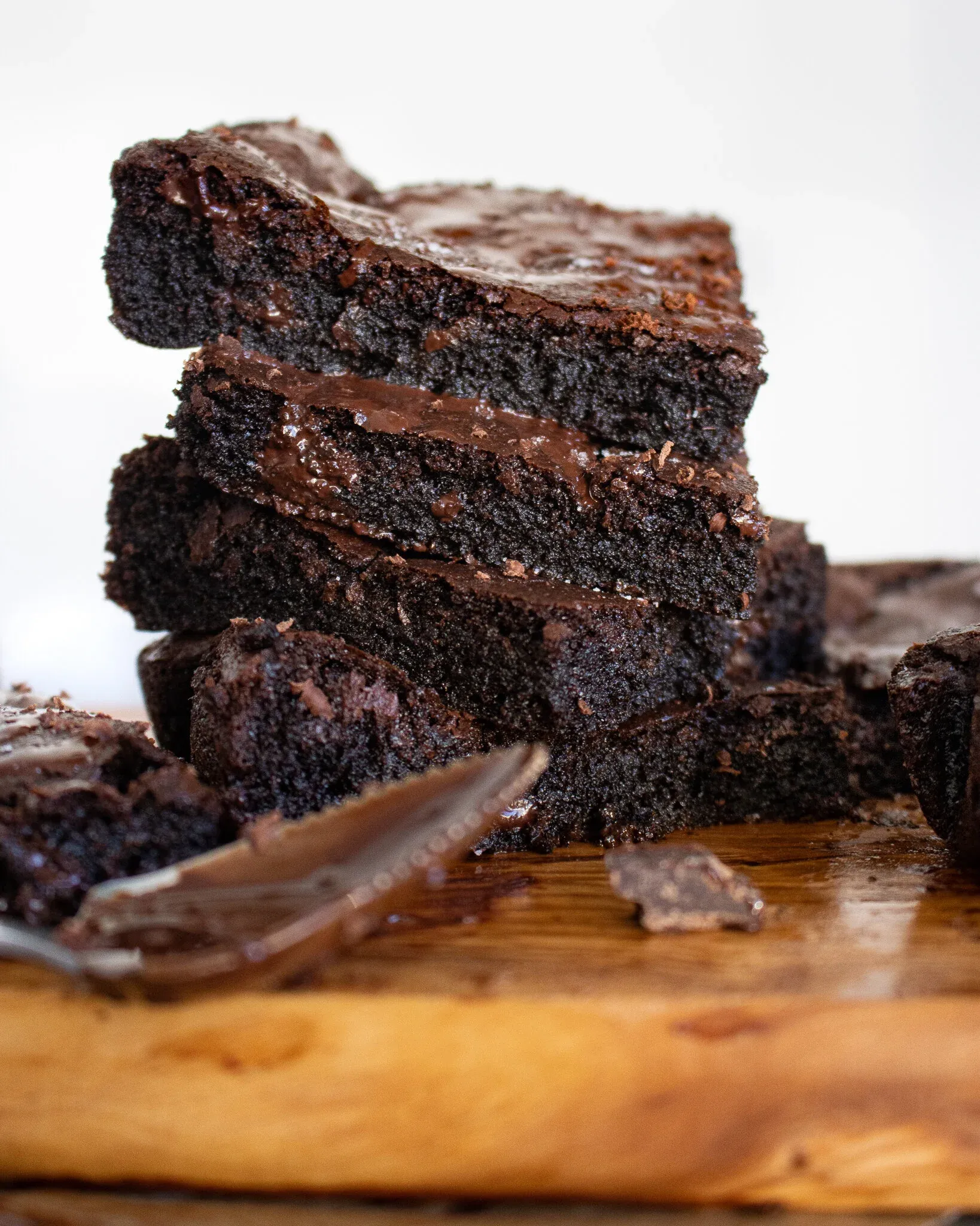 Stack of four Vegan Dark Chocolate Brownies balanced on a live-edge wood cutting board