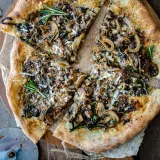 Overhead view of a sliced caramelized onion and mushroom pizza on a round wooden board over parchment paper