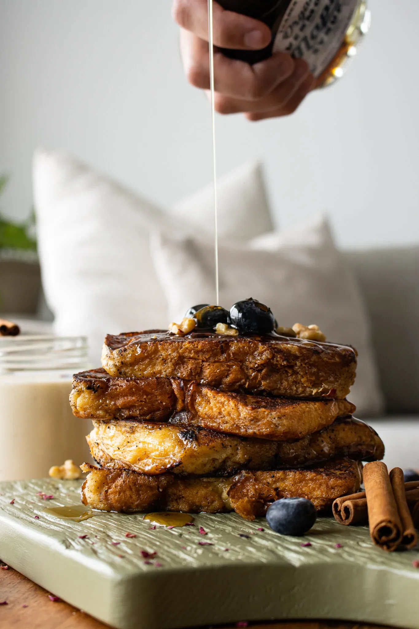 Portrait shot of a tall four-slice stack of deeply golden Coquito French Toast on a sage-green textured wood cutting board