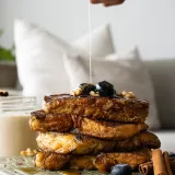 Portrait shot of a tall four-slice stack of deeply golden Coquito French Toast on a sage-green textured wood cutting board