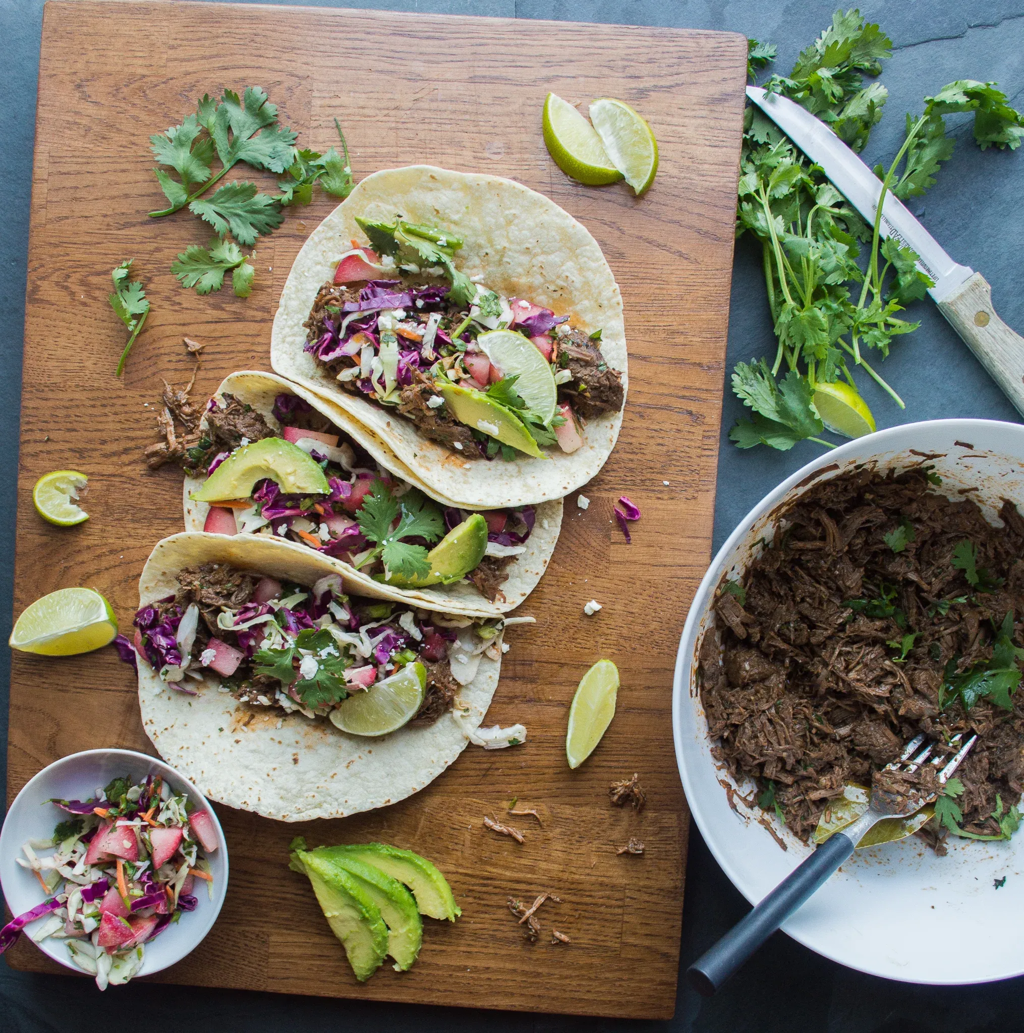 Three Slow Cooker Barbacoa Beef Tacos on flour tortillas arranged on a wood cutting board