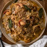 Overhead view of a large cream ceramic bowl of Sage and Browned Butter Shrimp Scampi with Ravioli on a wooden surface