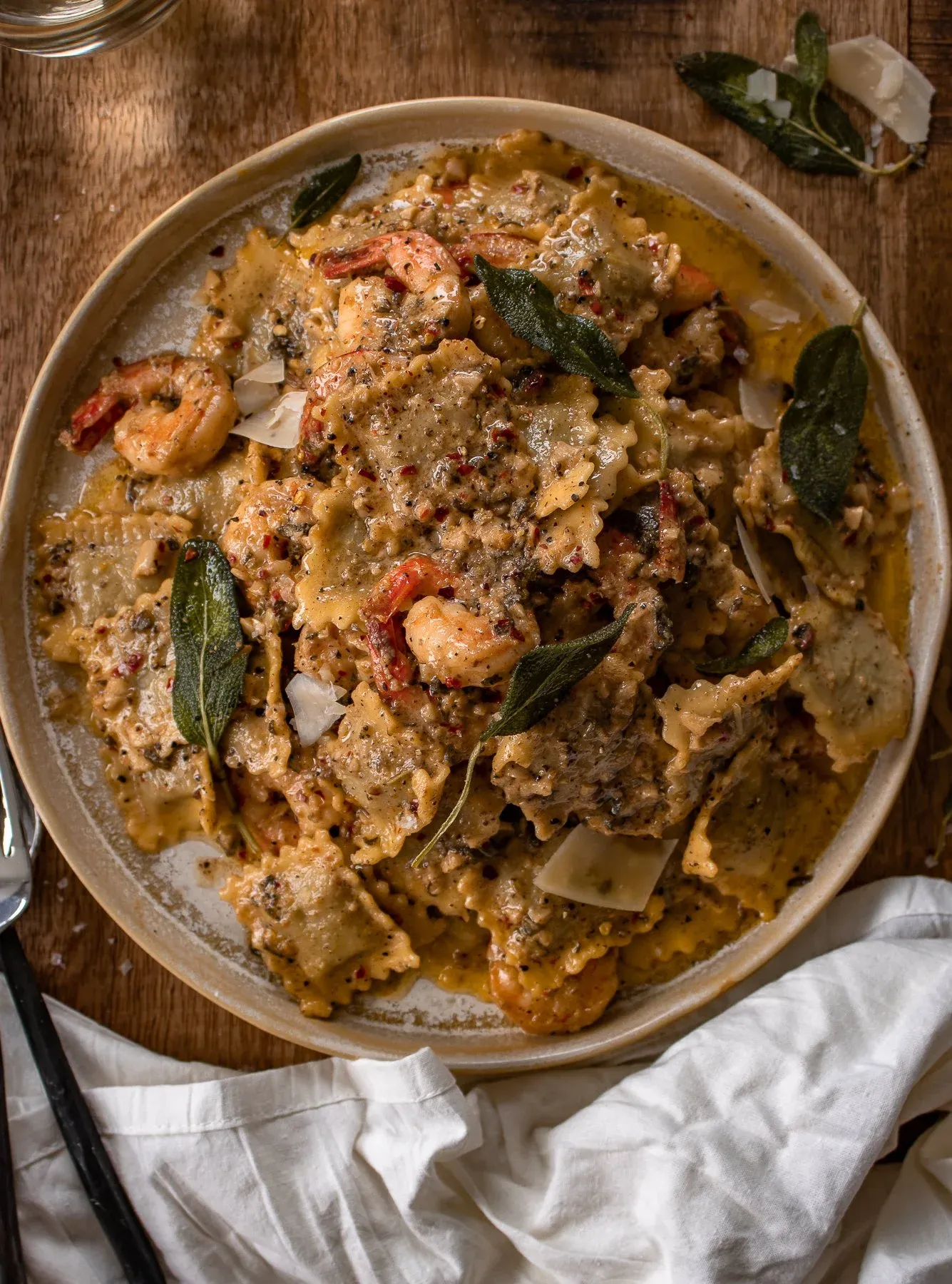 Overhead view of a large cream ceramic bowl of Sage and Browned Butter Shrimp Scampi with Ravioli on a wooden surface