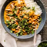 Overhead shot of a speckled matte blue ceramic bowl of Chickpea and Sweet Potato Stew on a white linen napkin over a dark wood surface