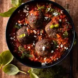 Four large herb-seasoned beef meatballs nestled in a deep, chunky spicy tomato sauce inside a black skillet