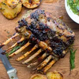 Herb crusted rack of lamb with frenched white rib bones standing upright on a warm wood cutting board