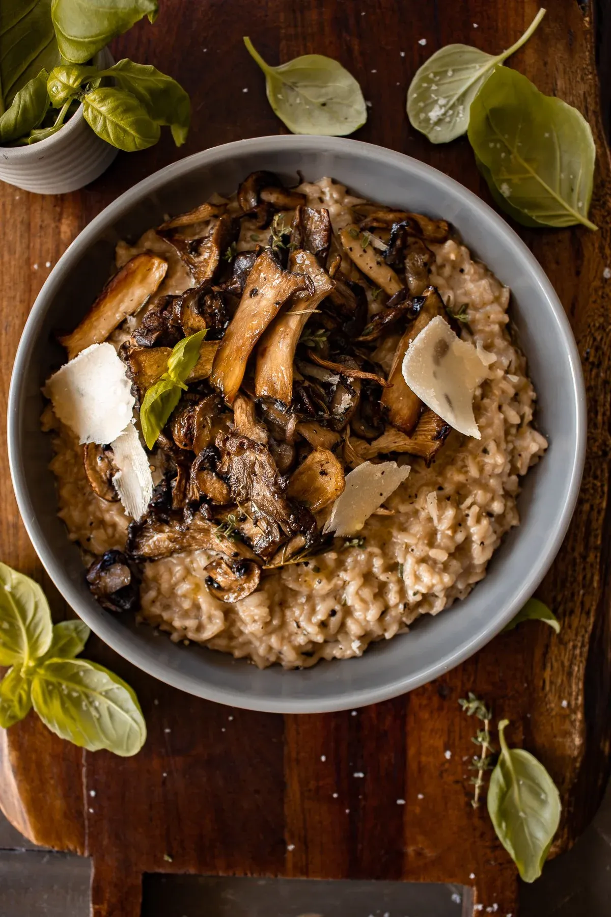 Overhead shot of a wide matte gray ceramic bowl of Creamy Parmesan Risotto with Roasted Thyme Mushrooms on a dark wood cutting board
