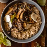 Overhead shot of a wide matte gray ceramic bowl of Creamy Parmesan Risotto with Roasted Thyme Mushrooms on a dark wood cutting board