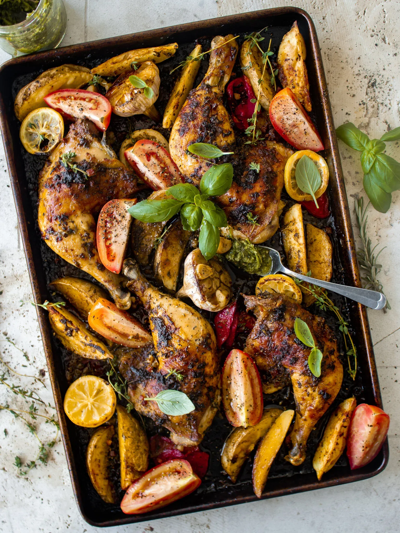 Overhead view of a dark sheet pan of Sheet Pan Dominican Roasted Chicken with Wasakaka on a light stone surface