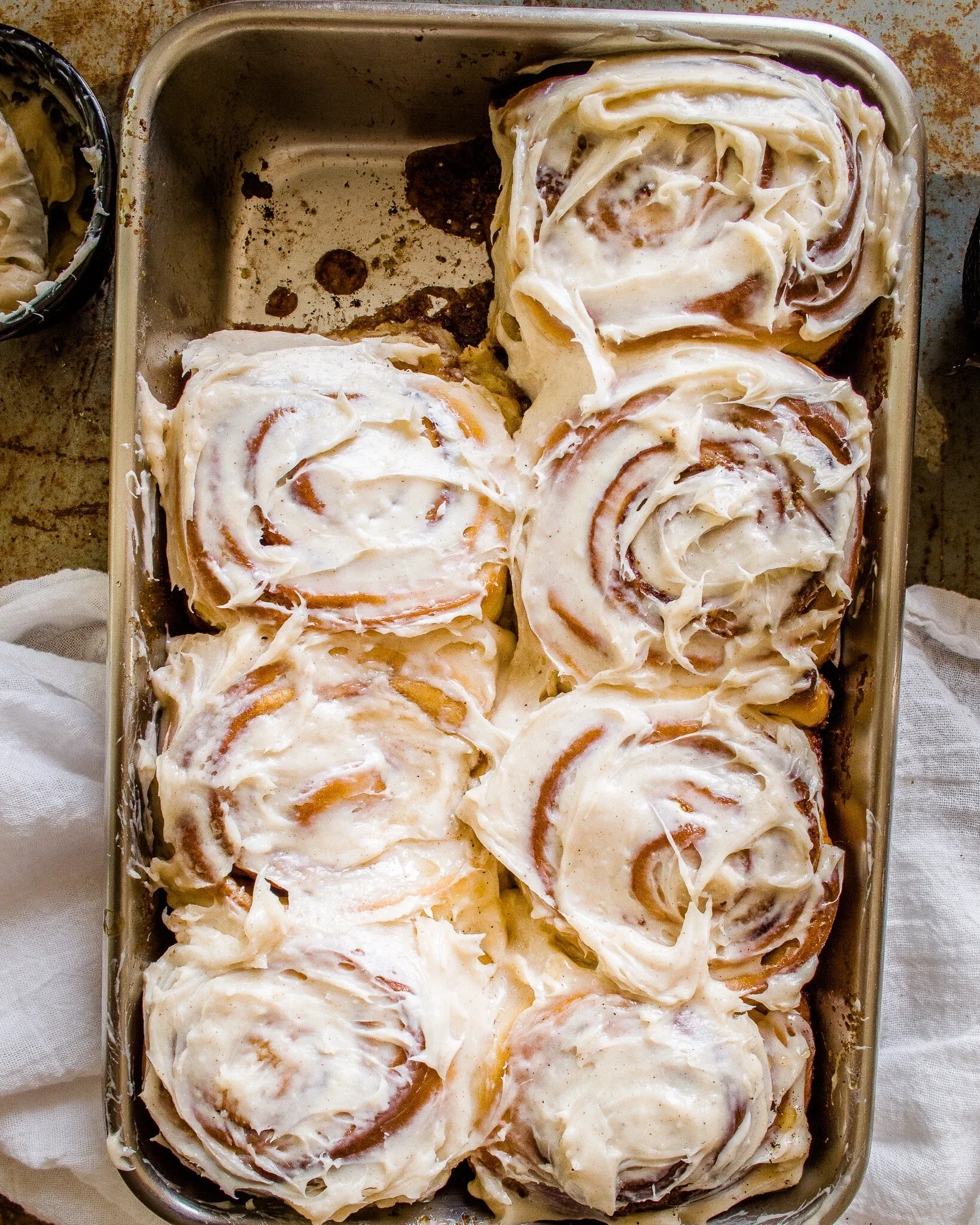 Overhead flat-lay of eight Brown Butter Cinnamon Rolls with Cream Cheese Frosting packed tightly in a worn silver metal baking pan