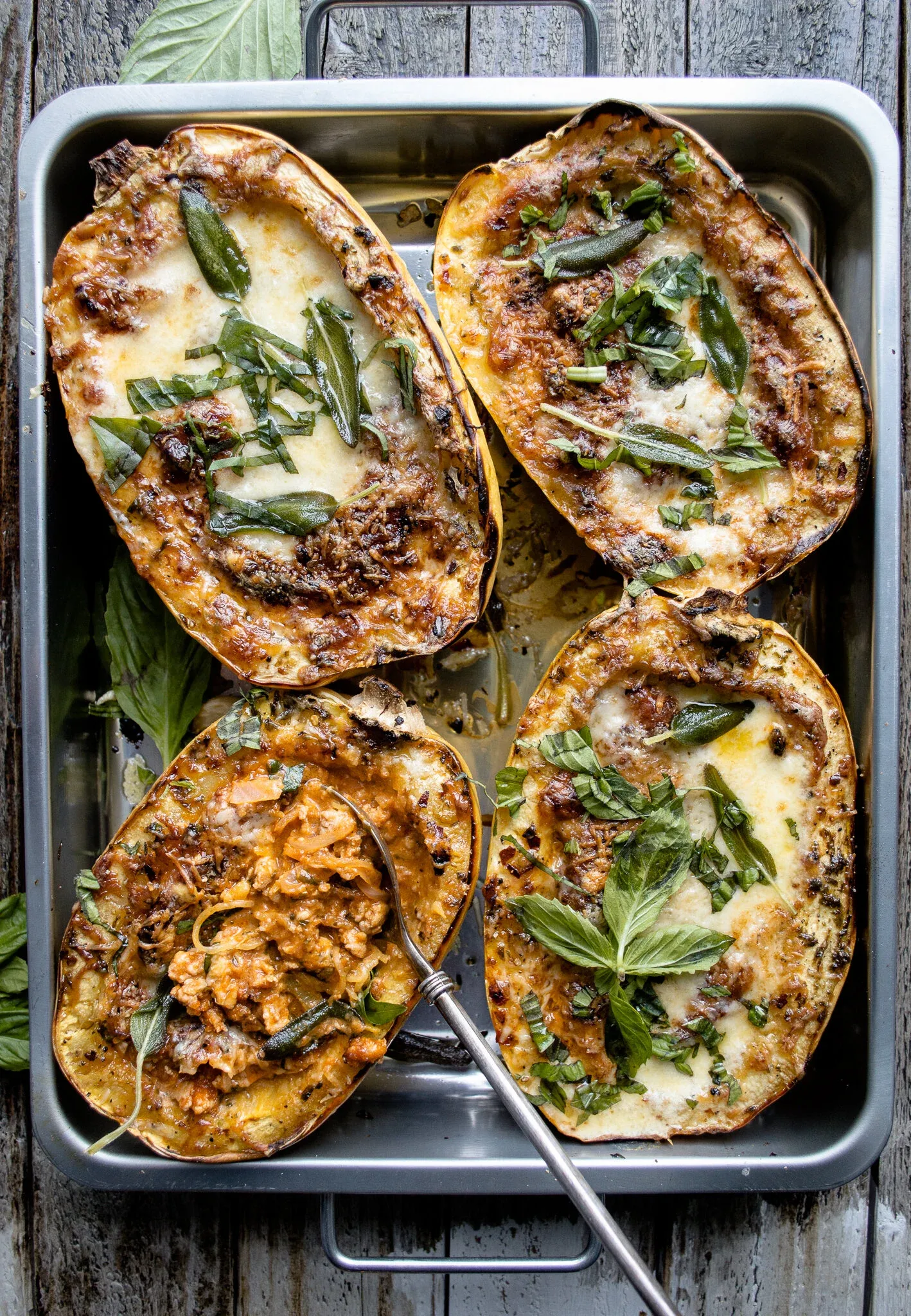Four halves of Stuffed Spaghetti Squash in a silver metal baking pan, overhead view on a rustic wooden surface
