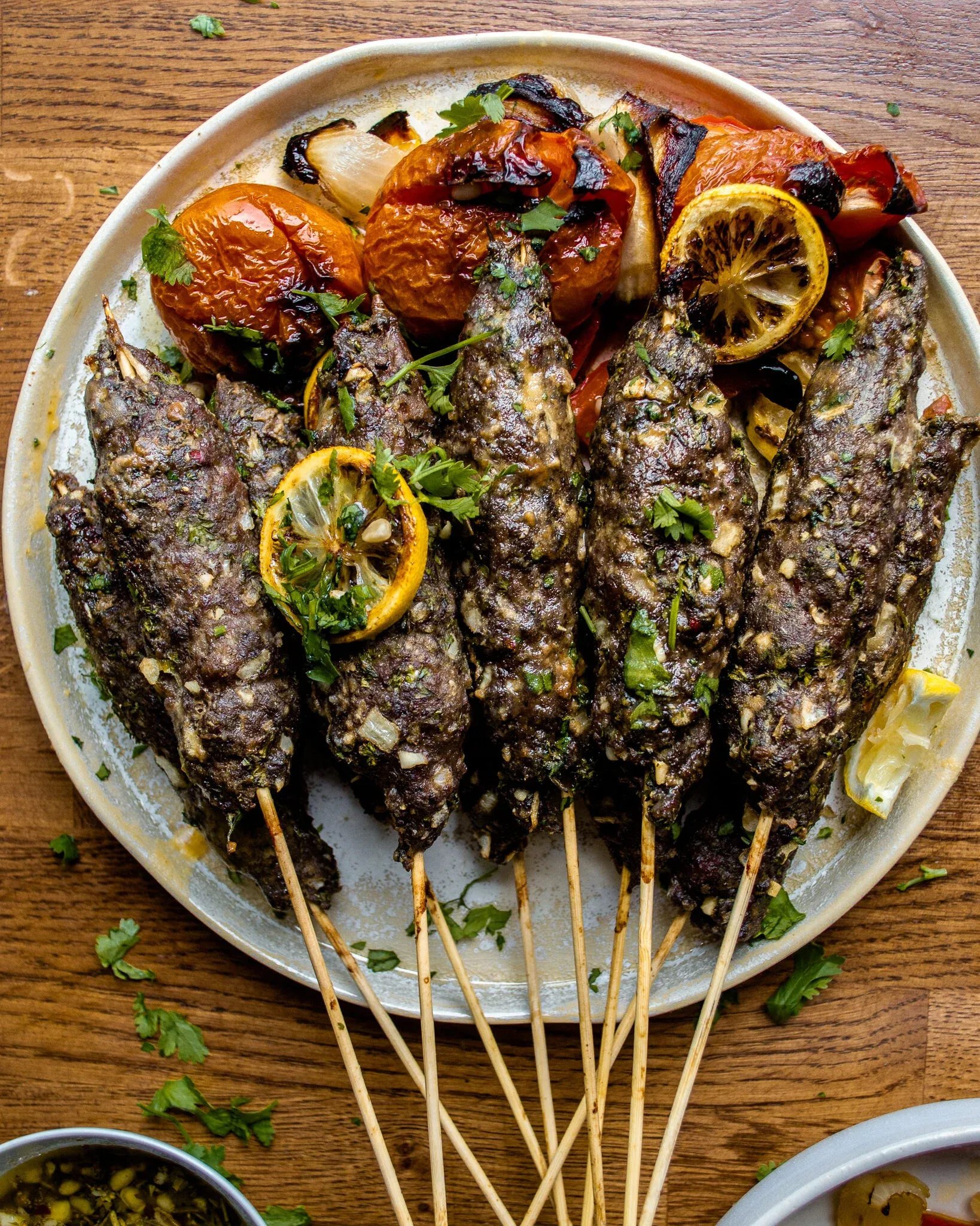 Six lamb and beef kabobs on wooden skewers arranged across a round speckled ceramic platter