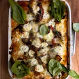 Spicy Chicken and Spinach Lasagna in a white ceramic rectangular baking dish with handles, overhead view on a wooden board