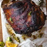 Whole puerco asado roast pork shoulder resting on crinkled parchment on a wooden surface