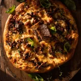 Short Rib and Mushroom Pizza presented whole on a round wooden lazy-Susan board