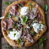 Overhead view of a whole Roasted Mushroom and Prosciutto Pizza on a rustic wooden board