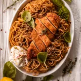 White oval serving dish of lemon pepper chicken pasta with burrata