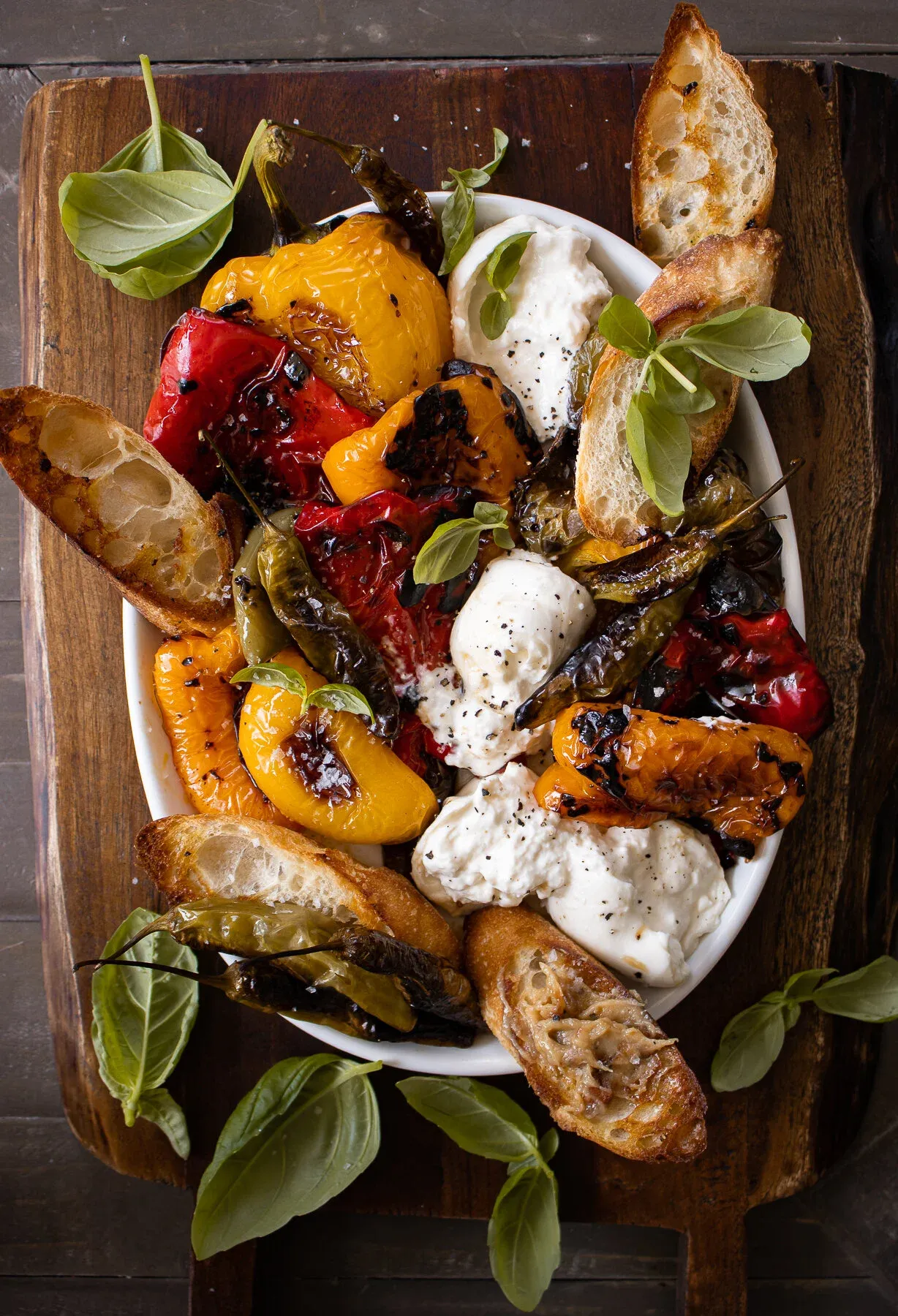 Overhead view of Roasted Peppers with Burrata and Garlic Spread in a white oval serving dish on a dark wooden board