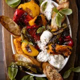 Overhead view of Roasted Peppers with Burrata and Garlic Spread in a white oval serving dish on a dark wooden board