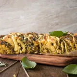 Pesto spinach and artichoke pull-apart bread served whole on a rectangular wooden board lined with parchment paper