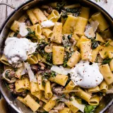 Overhead shot of One Pot Mushroom and Spinach Pasta in a large stainless steel skillet with wire handles on a white weathered wood surface