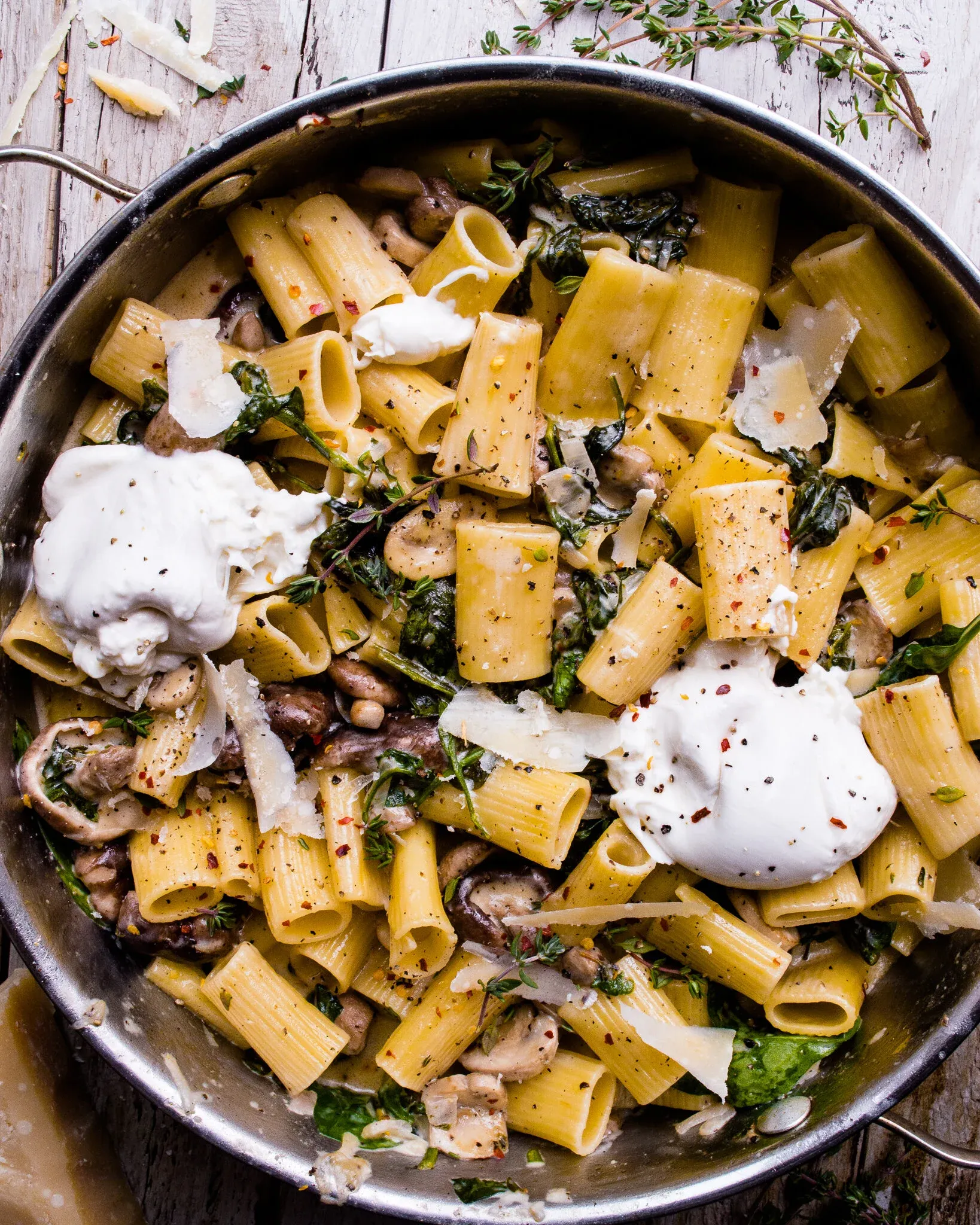 Overhead shot of One Pot Mushroom and Spinach Pasta in a large stainless steel skillet with wire handles on a white weathered wood surface